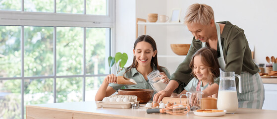 Little girl with her mother and granny rolling out dough in kitchen