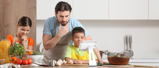 Thoughtful father with his children and tablet computer cooking in kitchen
