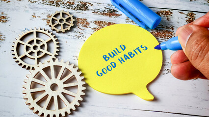 Build Good Habits Concept with Hand Writing on Speech Bubble Note Pad and Wooden Gear Wheels