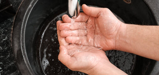 Man washing hands with soap in black sink, closeup