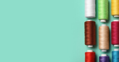 Set of colorful thread spools on turquoise background with space for text