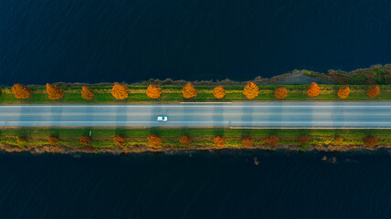Aerial view of road with car surrounded by trees and water at sunset