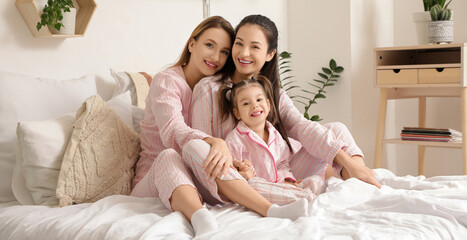 Young lesbian couple with their little daughter sitting in bedroom