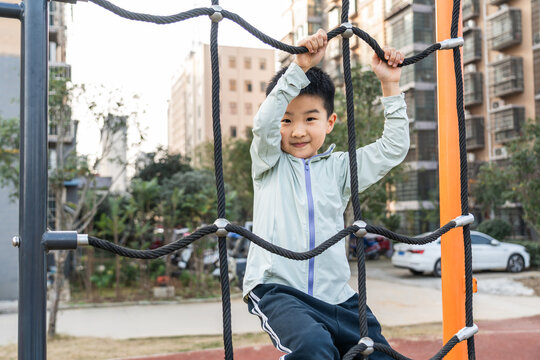 A young boy is climbing on a rope net in an outdoor park, showing his active and playful nature.