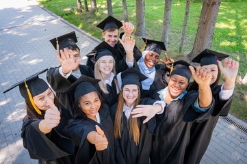 Obraz premium Students of different nationalities in graduation gowns wave their hands. 
