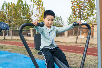 A young boy is using outdoor fitness equipment in a park, engaging in physical exercise.