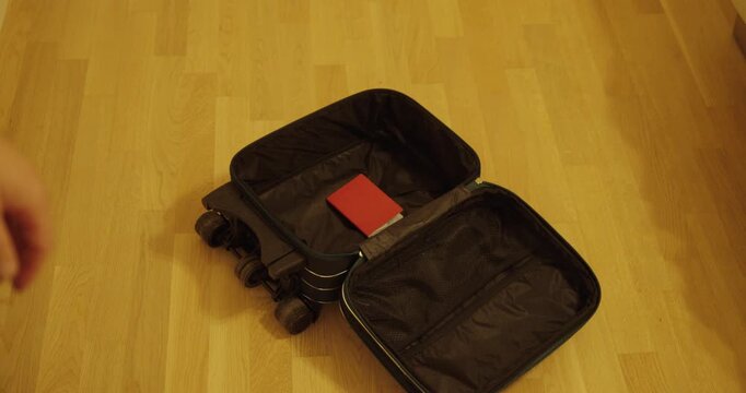 A person throws a red passport into an open suitcase before a trip, symbolizing preparation for travel, vacation, or an international journey.