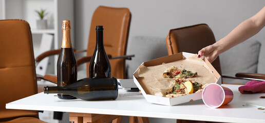 Female janitor taking pizza leftovers off table in office after New Year party, closeup