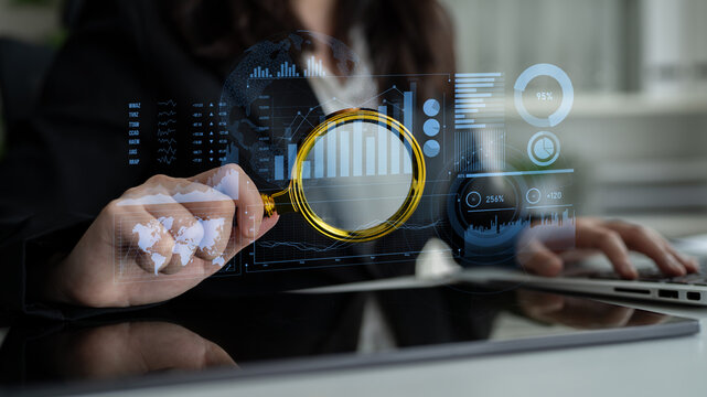A businesswoman uses a magnifying glass to analyze financial data in a modern office, highlighting digital graphs and statistics for effective decision-making. Scalp - Powered by Adobe