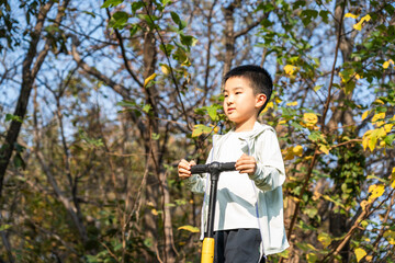 A young boy is having a good time outdoors amidst natural surroundings with trees and sunlight.