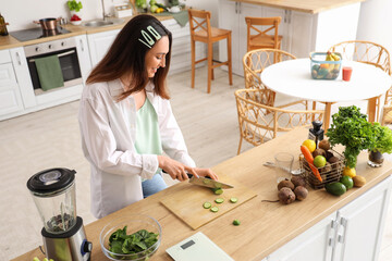 Young woman cutting cucumber for vegetable juice in kitchen