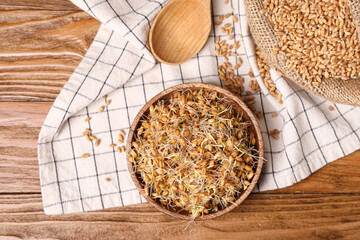 Bowl with sprouted wheat and spoon on wooden table
