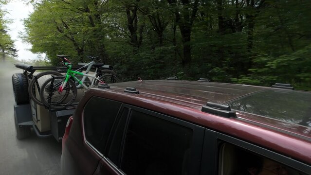 Family enjoys a camping adventure, with aerial view pulling a teardrop trailer on a narrow forest road with bicycles secured on the trailer for outdoor activities. - Powered by Adobe