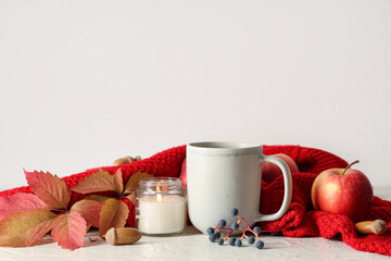 Composition with cup of green tea, autumn leaves and sweater on table near white wall