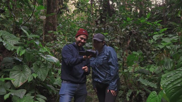 Two hikers pause on a dense forest path to share a fun moment while reviewing images together.