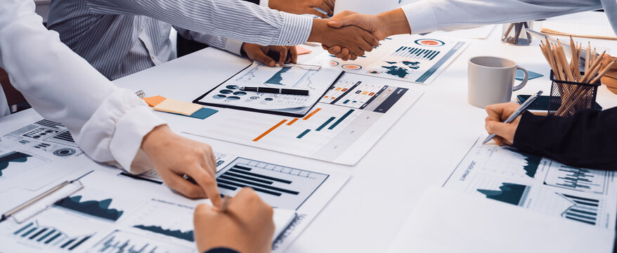 A diverse business team collaborates in a modern office setting, sharing insights through charts and graphs, emphasizing teamwork and strategic planning during their meeting. SACTR