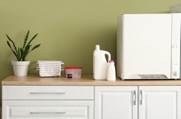 Drying machine and bottles of laundry detergent on wooden counter near green wall