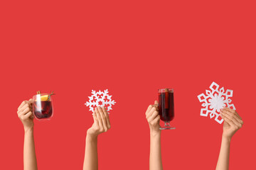 Female hands with decorative snowflakes, glass and mug of tasty mulled wine on red background