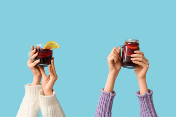 Female hands with cup and mug of tasty mulled wine on blue background