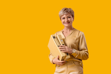 Mature businesswoman with folders on yellow background
