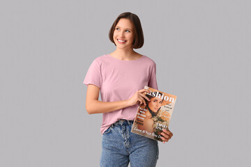 Young woman in stylish t-shirt with fashion magazine on grey background
