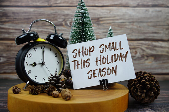 Festive holiday scene featuring a vintage alarm clock, pinecones, and miniature Christmas trees on a wooden base, with the text “Shop Small This Holiday Season” support for local businesses 