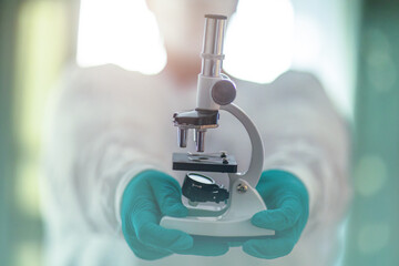 Scientist holding a laboratory microscope with gloved hands in a bright medical research environment