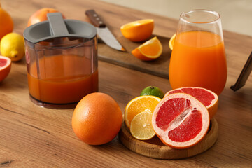 Wooden tray with tasty citrus fruits and jugs of fresh juice on table in kitchen, closeup