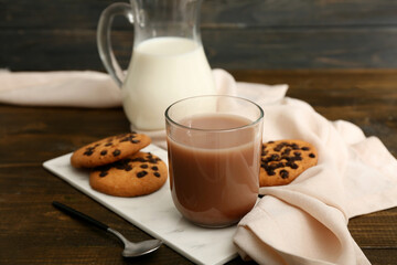 Glass of sweet chocolate milk and tasty cookies on wooden background