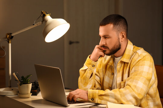 Thoughtful young man working with laptop in office at night