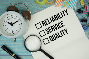 Reliability, Service and Quality text on a paper surrounded by office supplies, a magnifying glass,...