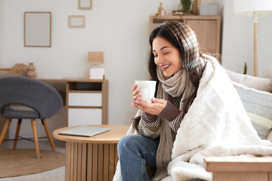 Young woman with warm plaid and cup of coffee at home on winter day