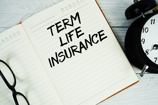 Notepad on a blue wooden table with the words "Term life insurance" with alarm clock and eyeglasses