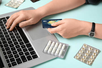 Female hands with modern laptop, credit card and pills on color background, closeup