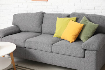 Interior of stylish living room with comfortable sofa and coffee table near white brick wall