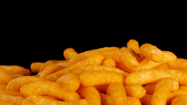 Cheese Puffs Dropping Onto Pile Against Black Background