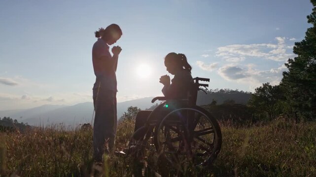 Silhouette elderly woman in wheelchair with his care helper praying to God on mountain sunset background.. Psychological medication treatment concept
