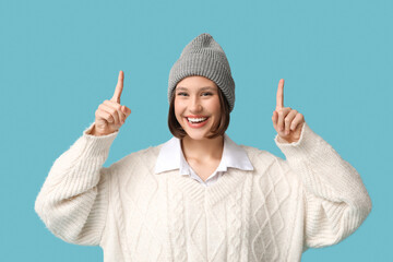Happy young woman pointing at something on blue background