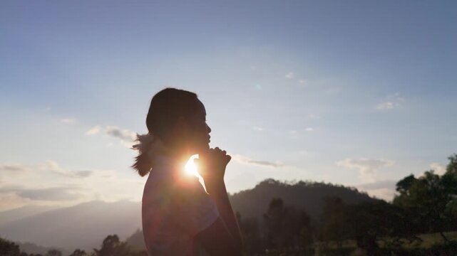 Silhouette girl praying and holding Christian cross for worshipping God on mountain at sunrise background. Christian, Christianity, Religion copy space background. Easter Sunday concept:
