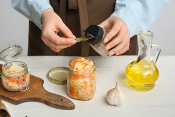 Woman taking bay leaf from jar on table in kitchen. Closeup