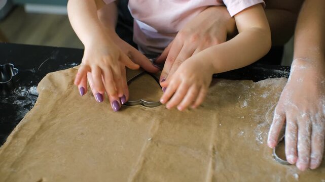 Close-up of hands from a mother and her daughters pressing and shaping ginger cookie dough, highlighting the shared learning and warm family participation in homemade baking concept