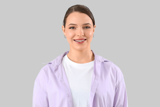 Young woman with dental braces smiling on light background