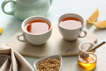 Cups of hot buckwheat tea, jar with honey and lemon slices on light background