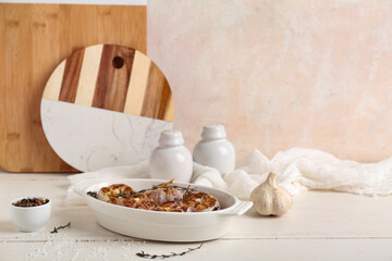Baking dish with garlic, rosemary, thyme and peppercorns on white wooden background