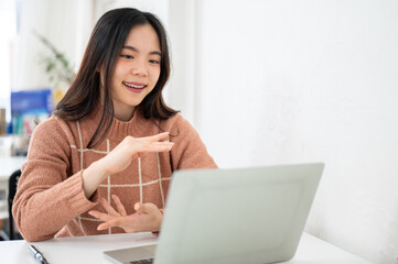 Obraz premium Asian woman explaining with hands and looking at a laptop on table in white room at office or cafe.