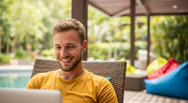 Young man smiling while working on laptop by pool nomad digital community enjoying outdoor remote work lifestyle