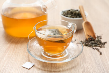 Glass cup of hot green tea and dried leaves on wooden background