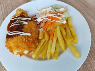 Chicken Katsu served with French fries and salad on a white plate