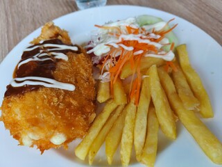 Chicken Katsu served with French fries and salad on a white plate