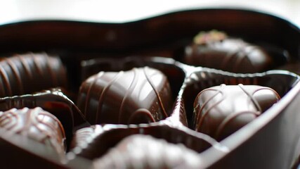 Close-up of assorted dark chocolates in a heart-shaped box with decorative drizzles and toppings, Valentine's day treat